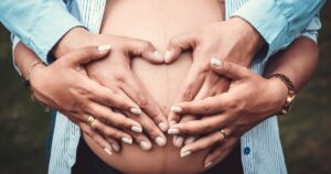 Couple holding hands on bare belly wearing blue shirts