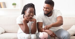 man and woman sitting on a couch with piggy bank on table in front of them